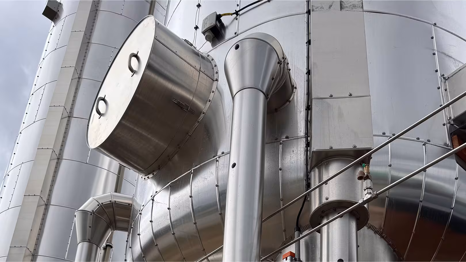 Witterungsfeste Außenisolierung großer Lager­tanks mit Aluminium­mantel und Anschluss­stutzen im Industrie­anlagenbau