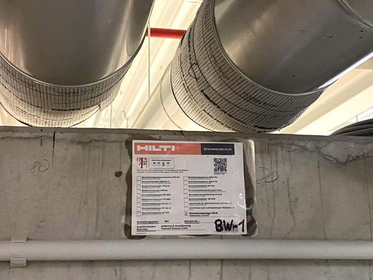 Brandschutzisolierung mit Hilti Brandwandschott CFS-B an Lüftungsrohren, Brandwanddurchführung mit Kennzeichnungsschild BW-1