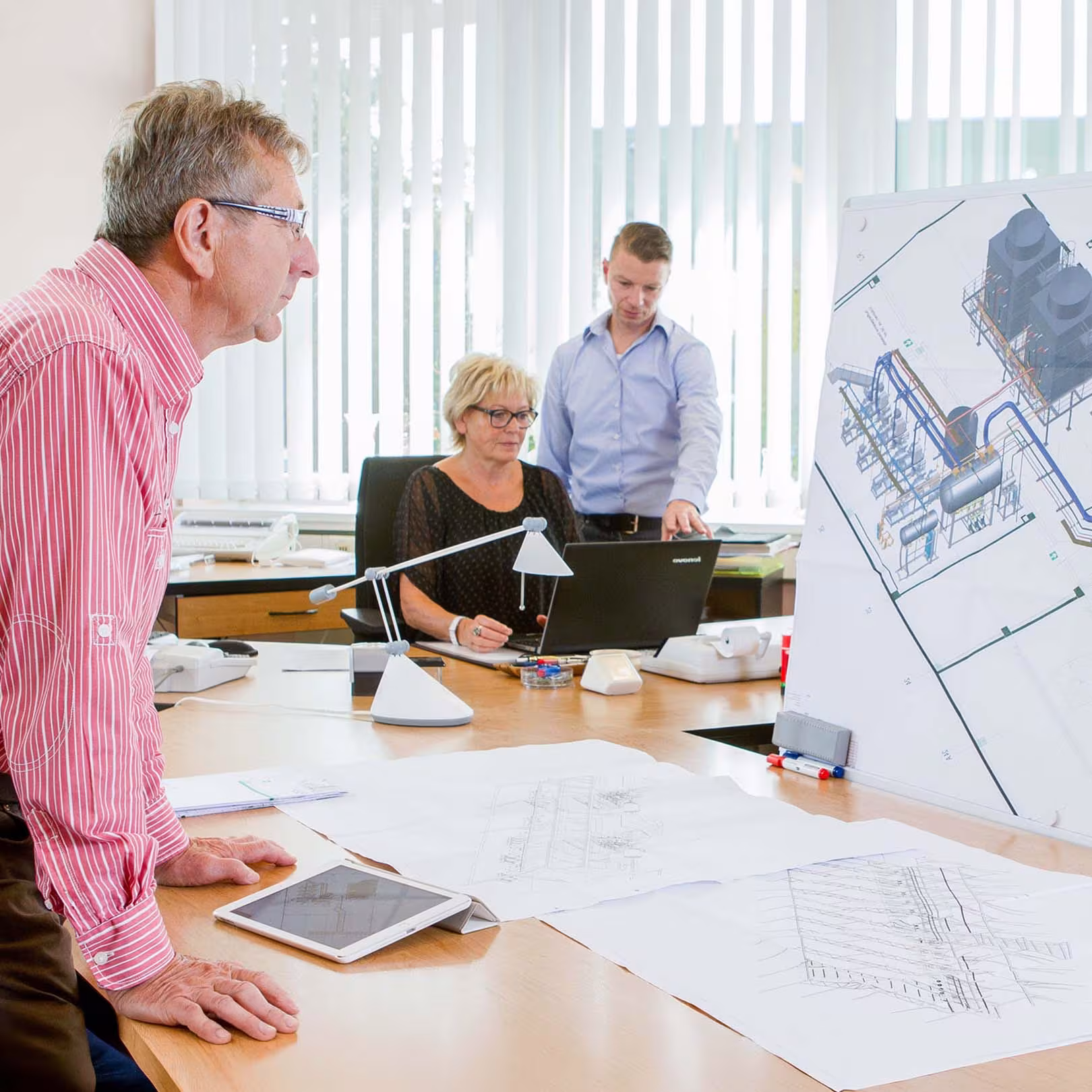 Drei IVS-Mitarbeiter besprechen im Büro die Projektplanung einer Industrieisolierung anhand von 3D-Zeichnungen und technischen Plänen einer Anlage